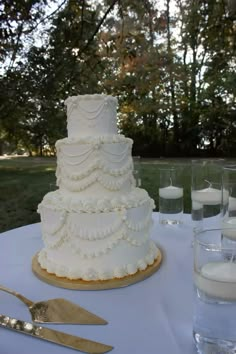 a white wedding cake sitting on top of a table next to silverware and candles