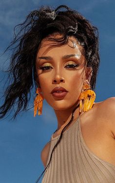 a close up of a person wearing large yellow earrings and a tan top with long hair