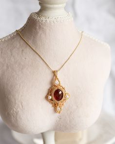 An artisan-made 14K gold-filled pendant, with a Garnet cabochon and faced cubic, is carefully hung from ball chain with a lobster clasp. This captivating pendant, boasting artwork of incomparable skill and a magnificent combination of red Garnet with an orange hue and translucent red Cubic, offers a perfect juxtaposition of poise and dynamism, making it an elitist piece of jewelry. The length of necklaces is approx. 24". Follow me on Instagram: @cubic_jewels Antique Cabochon Necklace With Round Pendant, Antique Cabochon Round Pendant Necklace, Gold Cabochon Teardrop Pendant Jewelry, Gold Cabochon Teardrop Pendant, Gold Pendant Necklace With Cabochon, Gold Cabochon Pendant Necklace, Yellow Gold Cabochon Teardrop Pendant Necklace, Victorian Pendant Necklace With Cabochon, Brass Cabochon Round Pendant Necklace