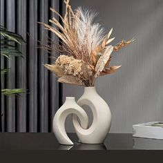 a white vase filled with dried plants on top of a black table next to a planter