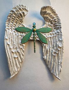 an angel wing ornament with a green dragonfly on it's back