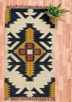 a black, yellow and red rug sitting on top of a wooden floor next to a plant