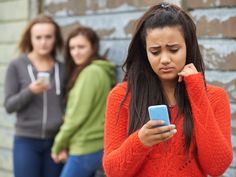 two girls looking at their cell phones while another girl looks on with her hand to her ear