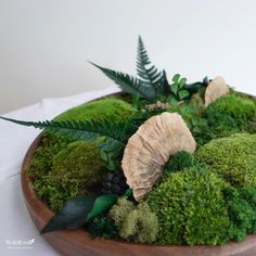 a wooden bowl filled with green moss and plants on top of a white table cloth