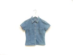 Vintage 90s womens little denim collared shirt. Six pearl snap button closures. Two chest pockets. Short sleeves. Fitted. Southwestern cowgirl bohemian vibes. A wild west top for a adventurous someone. Label: Real Clothes Jeans Fits Like: Marked womens S Color: Medium wash blue denim Fabrication: Cotton denim Condition: Great used condition, normal signs of wear 17" chest 15.5" shoulder 17" length 5" sleeve all measurements taken while garment lying flat This item comes from a pet & smoke free building For a look behind the scenes: + Instagram: brotherxiivintage Fitted Vintage Button-up Denim Top, Fitted Denim Blue Shirt For Summer, Fitted Denim Blue Collared Top, Fitted Light Wash Collared Shirt, Fitted Denim Summer Shirt, Vintage Medium Wash Denim Top For Summer, Medium Wash Fitted Short Sleeve Tops, Fitted Medium Wash Short Sleeve Denim Top, Fitted Short Sleeve Medium Wash Denim Top