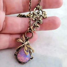 a hand holding a necklace with a pink stone in the center and gold filigrees on it