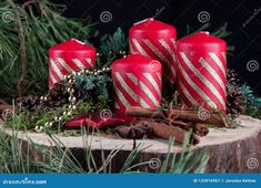 three red candles with gold stripes surrounded by pine cones and cinnamons on a tree stump