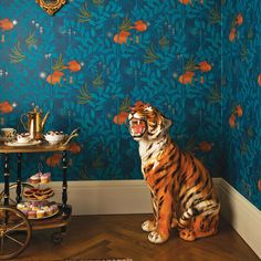 a tiger sitting on the floor in front of a wallpapered room with teapots