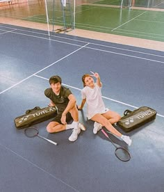 two people sitting on the ground with tennis rackets and bags in front of them