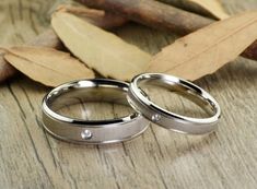 two wedding rings sitting next to each other on top of a wooden table with leaves