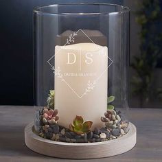 a white candle sitting on top of a wooden table next to a glass container filled with rocks and succulents