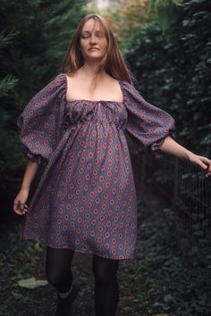 a woman in a dress is walking through the woods with her hand on her hip