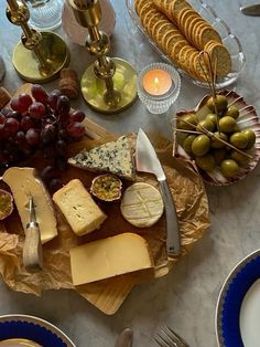 an assortment of cheeses, crackers and grapes on a table with silverware