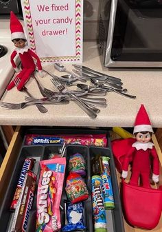 an elf with spoons, fork and candy bar in the drawer next to a sign that says we fixed your candy drawer