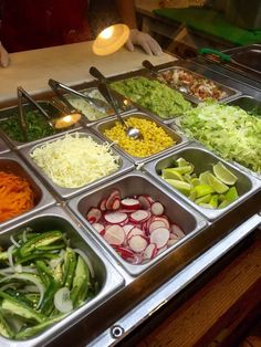 an assortment of salads in trays on a buffet table with utensils