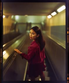 a woman standing on an escalator with her hand on the railing and looking up