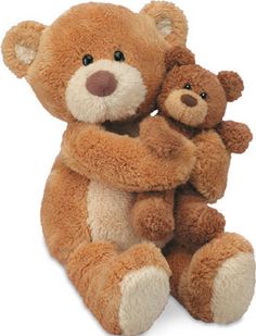 two brown teddy bears sitting next to each other on a white surface with one holding the other