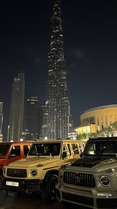 a group of cars parked in front of a tall building at night with the lights on