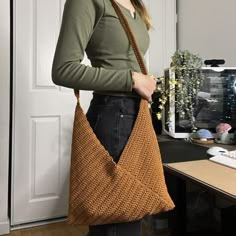 a woman standing in front of a computer desk holding a brown knitted handbag