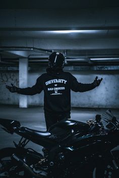 a man standing next to a motorcycle in a parking garage with his arms outstretched out