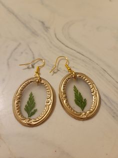 "These framed pressed flower earrings are handmade and use crystal clear hot glue to allow the flower to be seen inside the frame. The earring hooks are hypoallergenic, gold-plated stainless steel and come with a rubber back. The framed pressed flowers measure 1.25\"x1\" for the oval frame and 1\"x0.75\" for the rectangular frame. The flower color and frame shape can be customized." Handmade Gold Botanical Earrings, Botanical Style Gold Resin Jewelry, Gold Resin Earrings With Birth Flower Detail, Gold Resin Earrings With Birth Flower, Nature-inspired Gold Earrings With Pressed Flowers, Nature-inspired Gold Flower Earrings With Pressed Flowers, Gold Botanical Earrings With Pressed Flowers, Botanical Gold Earrings With Pressed Flowers, Botanical Gold Earrings With Birth Flower