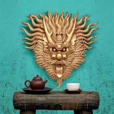 a teapot and cup sit on a wooden table with a dragon head above it