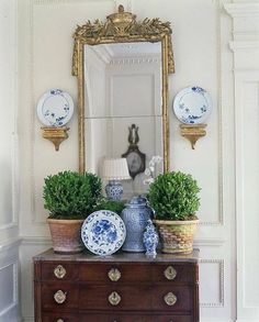 an old dresser with blue and white vases on it, next to a mirror