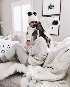 a woman holding a baby while sitting on top of a bed