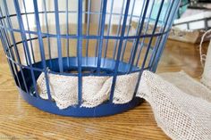 a blue birdcage sitting on top of a wooden table next to burlap