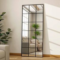 a mirror sitting on top of a wooden floor next to a white couch and potted plant