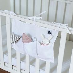 a white crib with a stuffed animal hanging from it's side and two pillows in the pocket