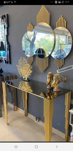 a console table with three mirrors on the wall and two sculptures in front of it