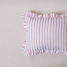 a red and white striped pillow with ruffles on the bottom, sitting on a beige surface