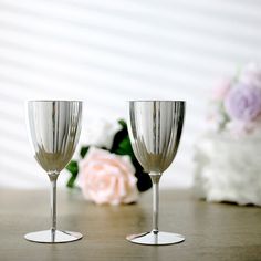 two wine glasses sitting on top of a table next to a bouquet of pink flowers