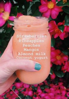 a hand holding up a jar filled with peaches and almond milk, surrounded by pink flowers