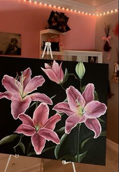 a painting of pink lilies on a black background with lights in the room behind it