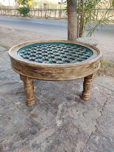 a wooden table sitting on top of a stone floor next to a tree and street