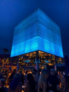 a group of people standing around in front of a building with blue lights on it