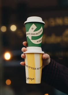 a person holding up a paper cup with writing on the bottom and inside it, in front of a blurry background