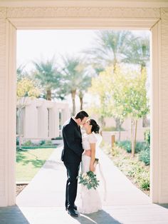 a bride and groom kissing in front of an archway