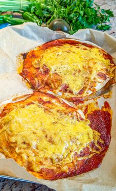 two pizzas sitting on top of a piece of wax paper next to some veggies