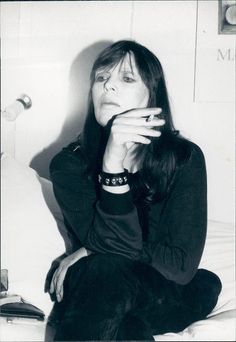 a black and white photo of a woman sitting on a bed with her hand in her mouth