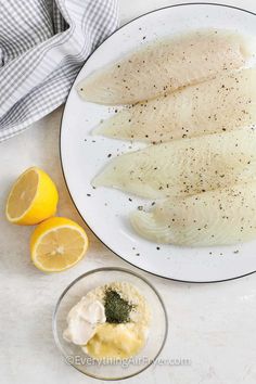 three fish fillets on a plate with lemons and seasoning next to it