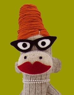 a sock monkey wearing glasses and a knitted hat is posed in front of a green background