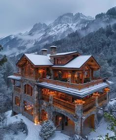 a large wooden house surrounded by mountains covered in snow and lit up with warm lights