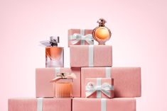 a stack of pink gift boxes with white bows and perfume bottles