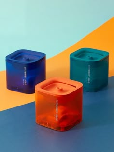 three different colored containers sitting on top of a blue and yellow surface with an orange stripe in the background