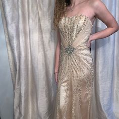 a woman standing in front of a white curtain wearing a gold dress with sequins on it