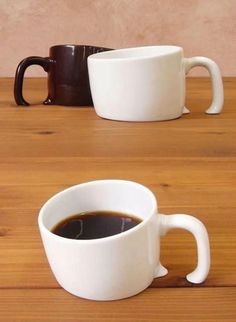 two coffee mugs sitting on top of a wooden table next to each other,