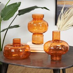 three orange vases sitting on top of a wooden table next to a white plant